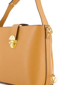 Tan læderhandtaske med struktureret design, hardware i guld-tone, klaplukning og en sideaccent med et rundt logo.