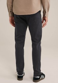 Jeans slim-fit gri închis, cu o textură netedă, buzunare pe spate și detalii de cusătură subtile, asociate cu adidași negri și albi.