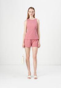 Top sin mangas de cuadros vichy rojos y blancos con pantalones cortos a juego, que presenta un diseño peplum. Combinado con sandalias blancas de tiras y un bolso pequeño.