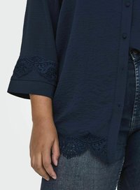 Top blu navy in tessuto texture, con bordo in pizzo lungo le maniche e l'orlo, design a bottoni, abbinato a jeans di denim.