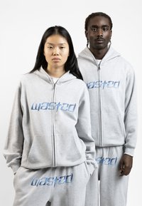 Grå hoodie og sweatpants sæt med blåt "wasted" logo, lynlås foran, kenguru-lommer og blød tekstur. Casual, afslappet pasform.