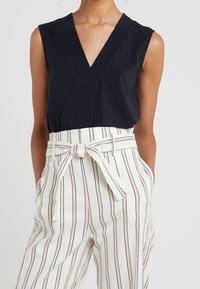Top sans manches bleu marine avec un col en V et un pantalon taille haute crème à rayures, doté d'une taille nouée et de lignes verticales. Tissu lisse et léger.