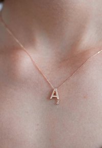Halskette aus Roségold mit einem Anhänger in Form des Großbuchstabens "A" und einem kleinen, hängenden Edelstein an einer zarten Kette.