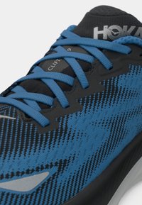 Scarpa da corsa blu e nera con tomaia testurizzata, sistema di allacciatura distintivo e suola ammortizzata. Presenta il marchio HOKA sulla linguetta.