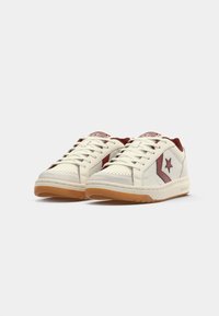 White sneakers with a slightly textured finish, featuring burgundy accents, a star logo, and a gum rubber sole. Laces are standard length.