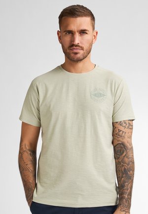 Light green short-sleeve t-shirt in a soft, textured fabric with a round neckline and a circular logo on the left chest.