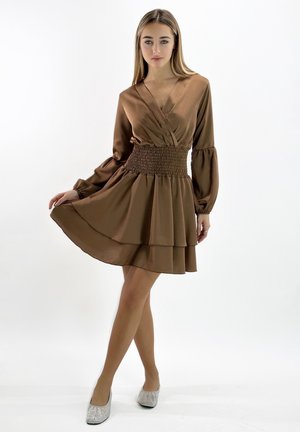 Robe marron à manches longues avec un décolleté en V, taille smockée et jupe superposée. Texture lisse avec un drapé élégant, associée à des ballerines argentées scintillantes.