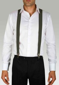 Chemise blanche avec un col, pantalon noir et bretelles vertes avec des clips en métal. La chemise a des manches longues et une fermeture à boutons.