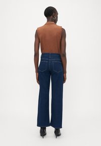 Blusa castanha sem mangas combinada com calças de ganga largas de cintura alta, de cor azul escuro. As calças têm dois bolsos traseiros e costura em contraste.