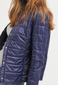 Navy quilted puffer jacket with a lightweight, glossy finish. Features snap buttons and a relaxed fit, suitable for casual wear.