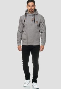 Haut de sweat à capuche gris zippé avec un col haut, un cordon de serrage et des accents en cuir. Associé à un jean slim noir et des baskets blanches.