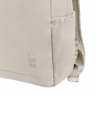 Zaino beige con tessuto testurizzato, tasca laterale in rete e logo stampato sulla parte anteriore. Design compatto con spallacci regolabili.