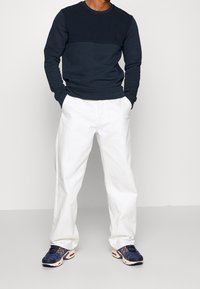 Suéter azul marino con diseño texturizado en la parte superior, pantalones blancos holgados y zapatillas azul marino con detalles en rosa.