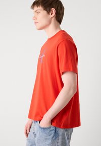 Červené bavlnené tričko s okrúhlym výstrihom. Na prednej strane sa nachádza modré logo Calvin Klein. Strih je voľný, rukávy sú krátke a materiál je hladký.