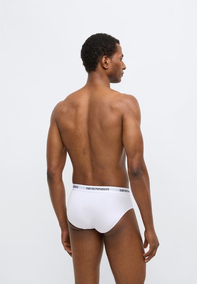 Slip en coton blanc avec une ceinture noire portant le logo "Emporio Armani". Texture lisse, coupe ajustée, design simple sans motifs.