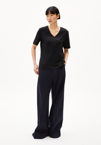 Zwart T-shirt met korte mouwen en een V-hals, gecombineerd met wijde marineblauwe broek. De stof lijkt soepel en lichtgewicht te zijn.