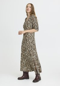Robe maxi en imprimé léopard avec des manches courtes, un col en V profond et des fentes sur les côtés ; portée avec des bottines à talons noires. Tissu lisse et léger.