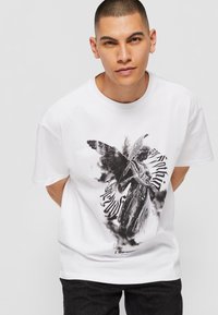 Hvid bomulds-T-shirt med et sort-hvidt grafisk motiv af en engel og tekstdesign, korte ærmer og rund hals.