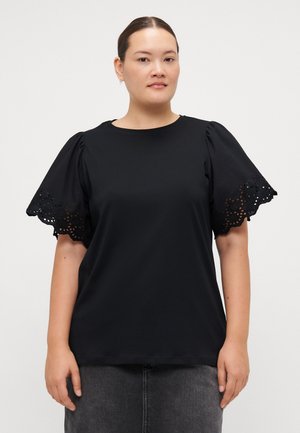 Svart kortermet topp med blonde detaljer på ermene, rund halslinning, myk stoff og avslappet passform. Brukt sammen med et mørkegrått skjørt.