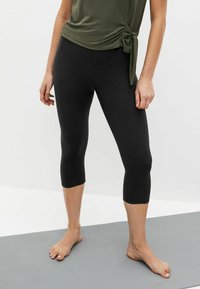 Fekete capri leggings rugalmas anyagból, sima textúrával, testhezálló dizájnnal, amely a térd alatt végződik.