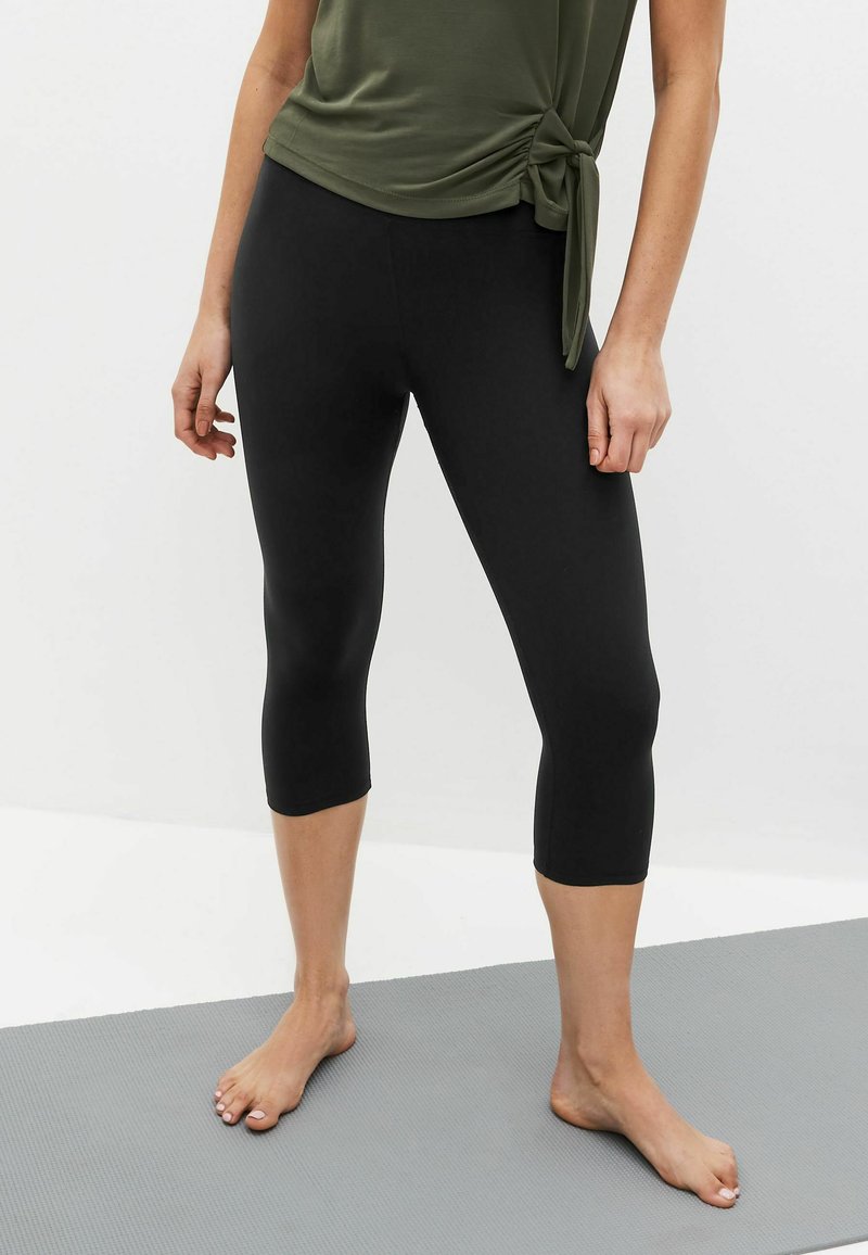 Fekete capri leggings rugalmas anyagból, sima textúrával, testhezálló dizájnnal, amely a térd alatt végződik.