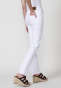 Biezi balti džinsi ar šauru piegriezumu un smalkiem izšūtiem akcentiem sānos. Apvienoti ar melniem siksnu sandāliem ar augstu papēdi.