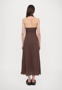 Brun, stroppeløs kjole med en tettsittende bodice og flytende skjørt, laget av lett stoff, sammen med chunky svarte platå sko.