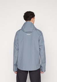 Wasserfeste graue Jacke mit Kapuze, gerade geschnitten, lange Ärmel und glatter Textur. Auf dem Rücken ist das Logo "MAMMUT" zu sehen.
