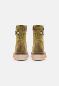 Stivali alla caviglia in suede verde oliva con finitura testurizzata, dotati di hardware argentato e una suola stratificata con un accento in legno naturale.