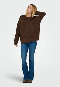 Brun strikket sweater med løs pasform og lange ærmer, parret med blå storeslåede jeans og brune ankelstøvler. Simpelt, afslappet design.
