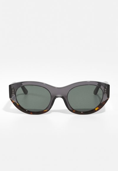 Sunglasses with a grey tortoiseshell frame, dark green lenses, and an oval shape. Features angular detailing on the temples.