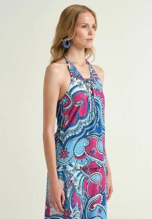 Femme portant un haut sans manches à col halter coloré avec des motifs cachemire bleus et roses, assorti à une jupe et des boucles d'oreilles hoop bleues.