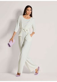 Witte jumpsuit met een strikdetail op de taille, driekwartmouwen en brede benen. Gecombineerd met lavendel kleurige hakken en een bijpassende clutch.