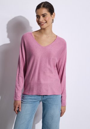 Haut rose clair à manches longues avec un décolleté en V et une coupe décontractée, associé à un jean large bleu clair. Texture lisse et design décontracté.