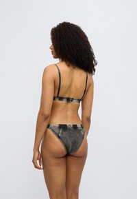 Σετ σουτιέν και μπικίνι με μοτίβο μαύρου τζιν, με ρυθμιζόμενους ιμάντες και χαμηλή μέση. Διαθέτει φθαρμένη υφή και διακριτικές ραφές.