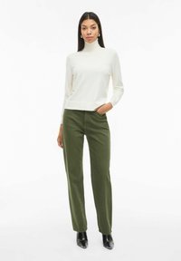 Suéter de cuello alto crema combinado con pantalones rectos verde oliva. El conjunto presenta una textura suave y un diseño simple y moderno.
