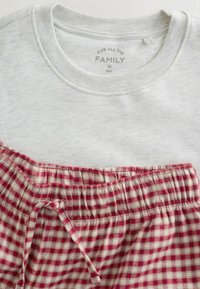 Sivý sweatshir s okrúhlym výstrihom nad červenými károvanými pyžamovými šortkami; šortky majú elastický pás a detaily so šnúrkou.