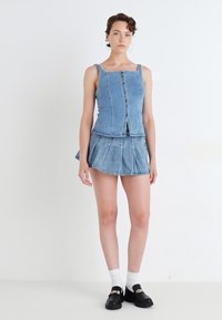 Denim öltözet, amely ujja nélküli, elől gombos topból és hozzá illő szoknyából áll. Világoskék szín, sima textúra és bővülő fazon.
