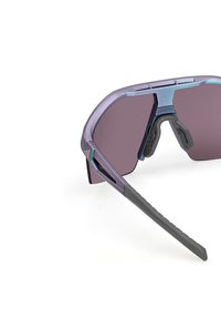 Sporter solglasögon med en lila metallram, grå gummidetaljer, stora grå linser och strukturerade svarta skalmar för bättre grepp.