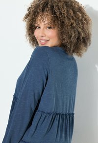 Blaues Langarmoberteil aus strukturiertem Stoff, mit gerafften Akzenten an der Taille und den Ärmeln. Weiches, lässiges Design mit einer lockeren Passform.