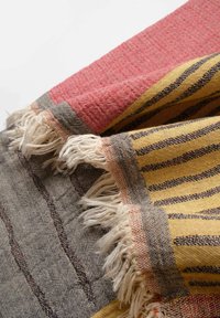 Woven textile featuring stripes in yellow, black, and red. Edges have a fringed texture with a soft neutral gray background.