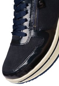 Donkerblauwe sneaker met gestructureerde stof, glanzende lakleren accenten, marineblauwe veters, zijrits en witte rubberen zool met profiel.