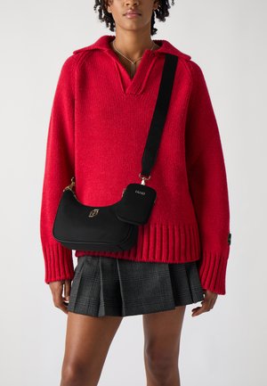 Maglione rosso lavorato a maglia con colletto, abbinato a una borsa a spalla nera con dettagli dorati e una piccola pochette aggiuntiva; gonna scozzese.