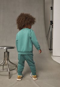 Türkiissinine pehme kangaga dressipluusi ja pükste komplekt. Vahvliääristega varrukad ja servad, kombineeritud mitmevärviliste tossudega.