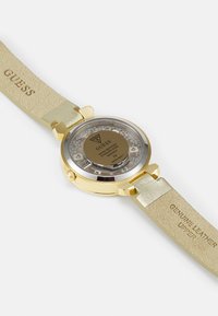 Goldfarbene Uhr mit klarem Gehäuse, echtem Lederarmband und goldenen Akzentdetails. Mit transparentem Rückenteil, das die inneren Mechanismen zeigt.