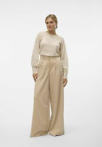 Beige bredde ben bukser parret med en struktureret, lys beige langærmet top, der har et subtilt mønster og en afslappet pasform.