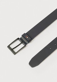 Tumši zils ādas jostas siksna ar melnu metāla sprādzi, šuvju detalizāciju un nelielu logotipu tuvumā sprādzei. Plakana, gluda dizains.