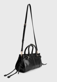 Zwarte leren handtas met dubbele handgrepen, afneembare schouderriem, hardware in goudkleur en een gladde afwerking met decoratieve stiksels.