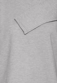 Chemise grise à manches longues avec une texture côtelée, présentant un col arrondi et une seule manche visible, indiquant un design décontracté.