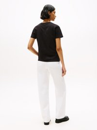 T-shirt noir à manches courtes, pantalons blancs à jambe droite, chaussures noires, texture de tissu lisse, vu de dos, design minimaliste.